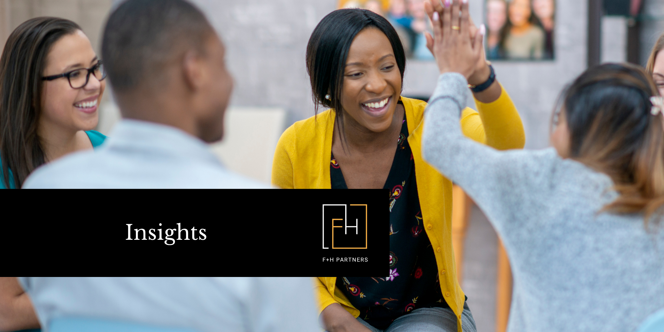 A group of colleagues in a collaborative meeting share a high-five, smiling and engaged.